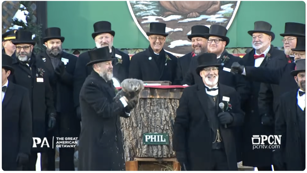 Punxatawney Phil being held aloft by the dudes in top hats at Gobbler's Knob, who are grinning in spite of the fact that Phil saw his shadow and predicted 6 more weeks of winter.